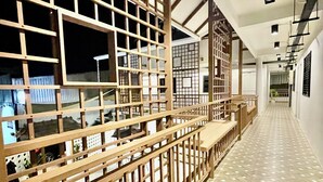 A corridor with a wooden lattice partition, tiled flooring, and a view of a building with large windows. - Secret Corner Boutique Stay  (Chiang Rai)
