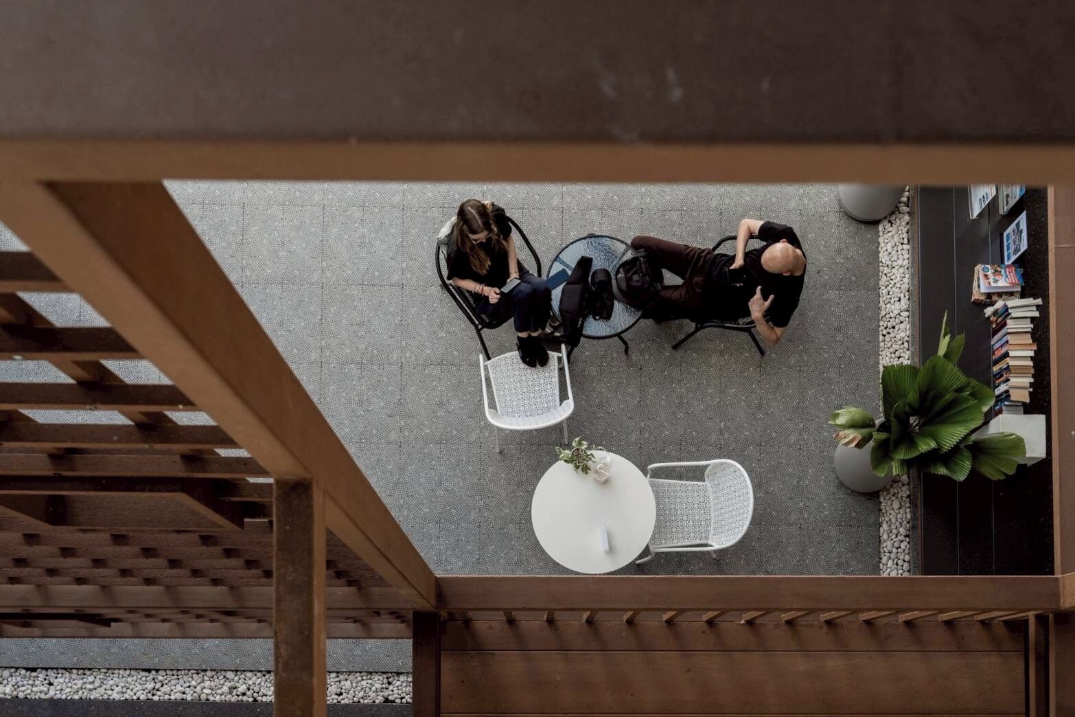 An overhead view of a café with a wooden pergola, white chairs, and a round table.