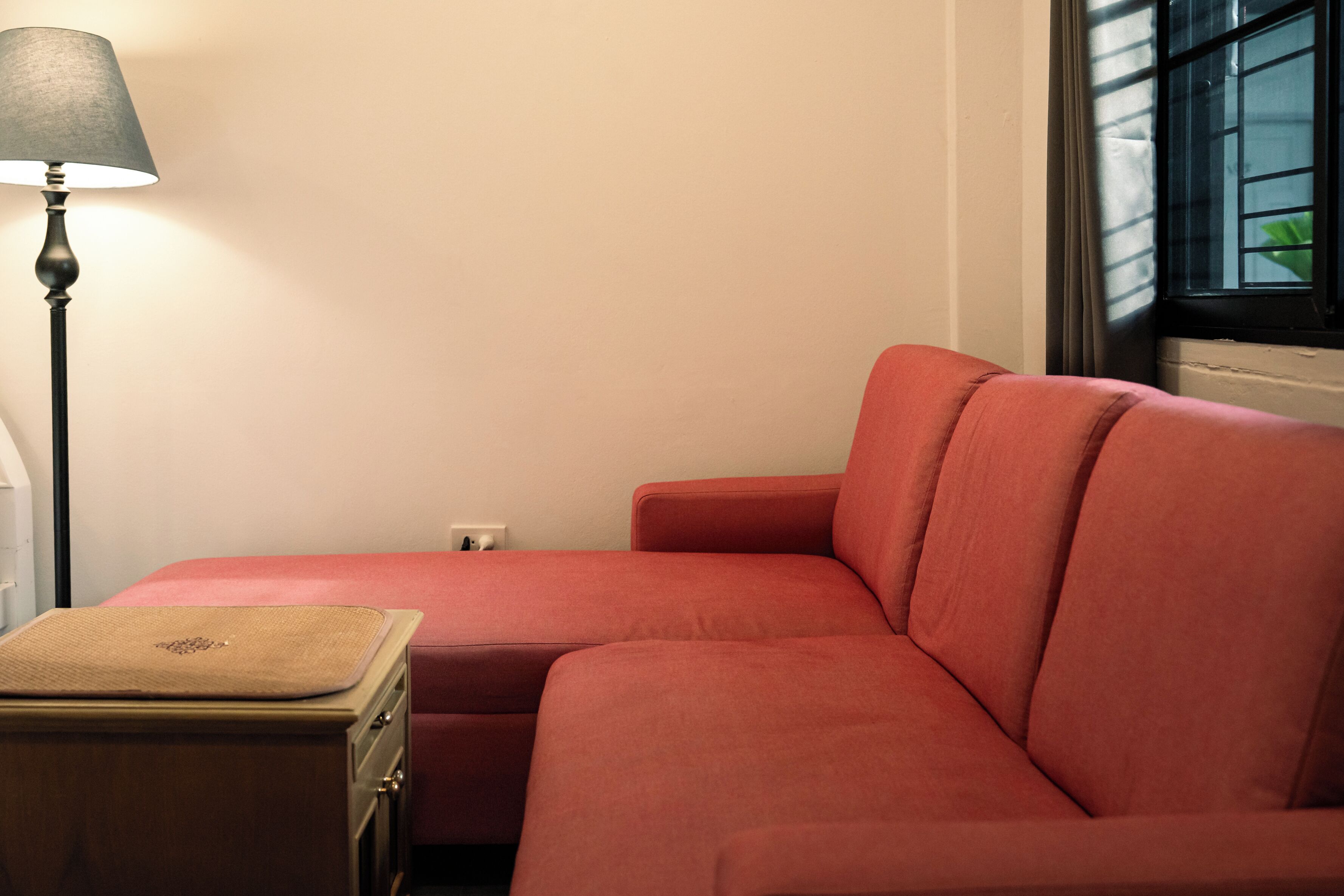 A room with a red sofa, a lamp, and a window with blinds.