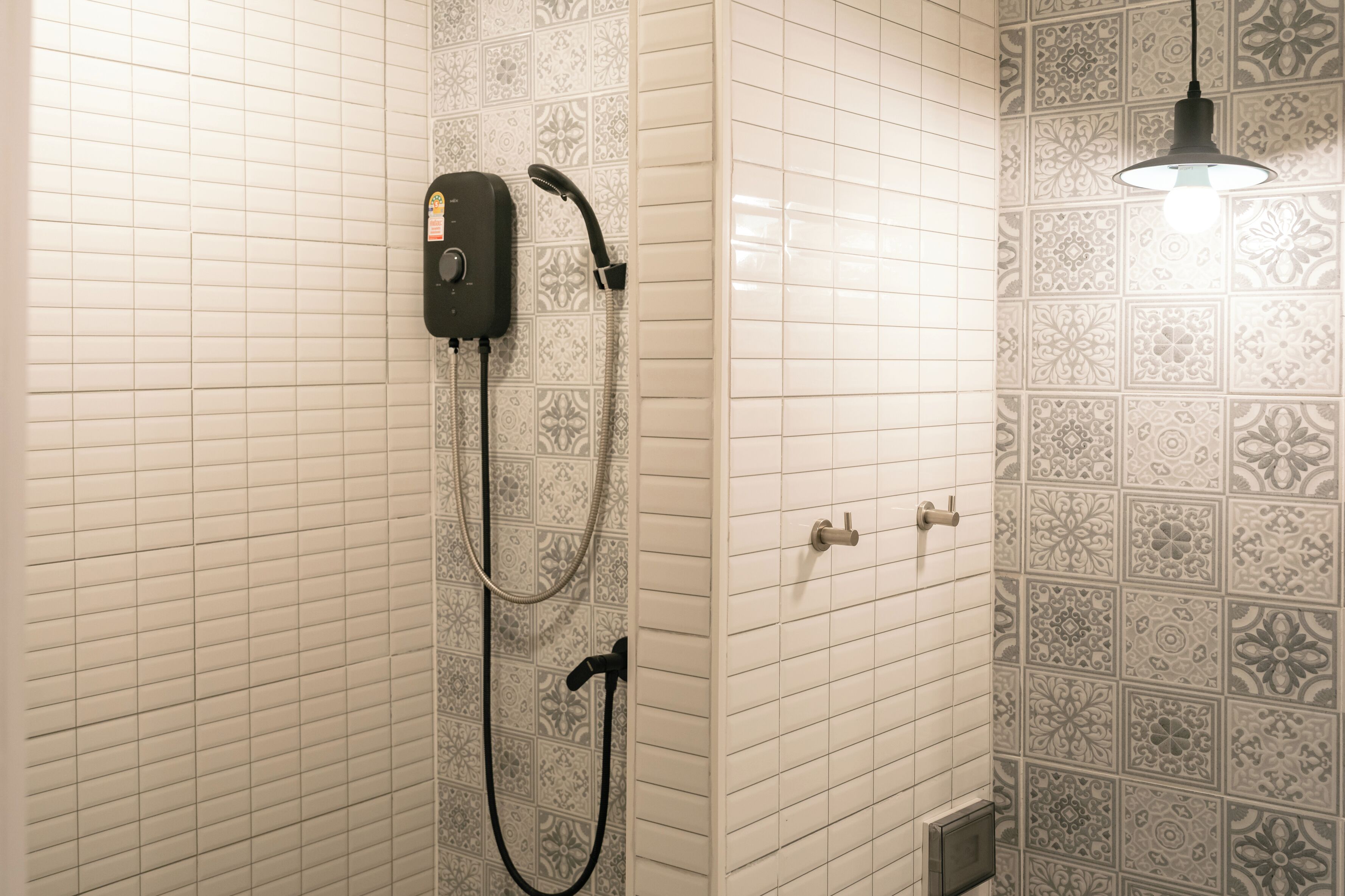 Un baño con ducha, un cabezal de ducha de mano, un panel de control en la pared y un diseño de azulejos estampados.