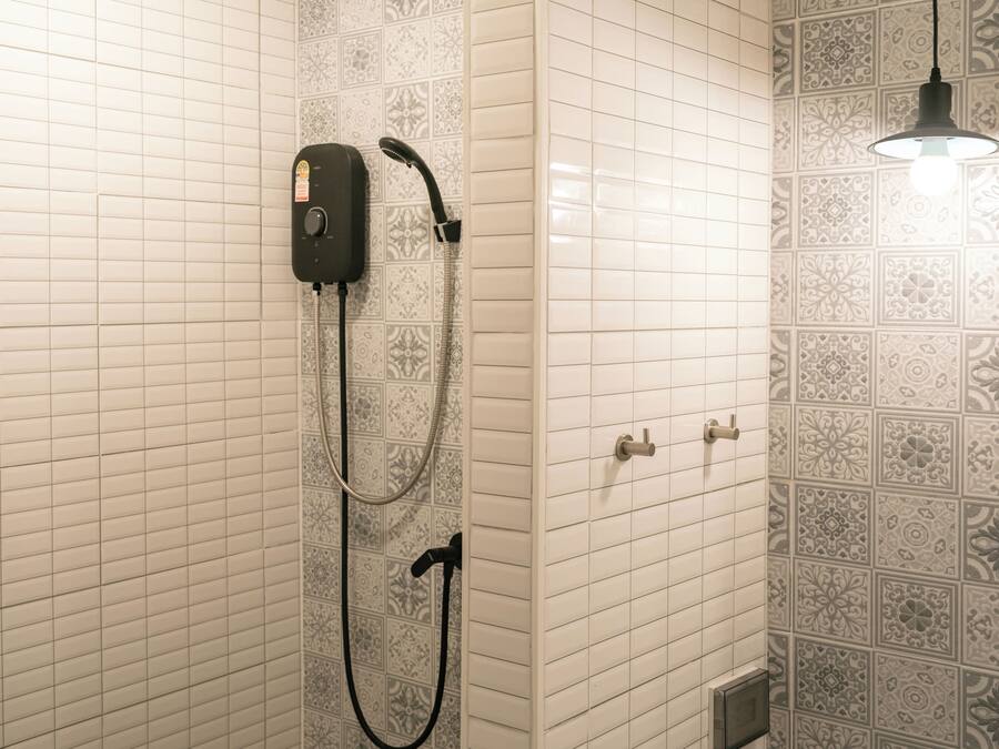 Un baño con ducha, un cabezal de ducha de mano, un panel de control en la pared y un diseño de azulejos estampados.