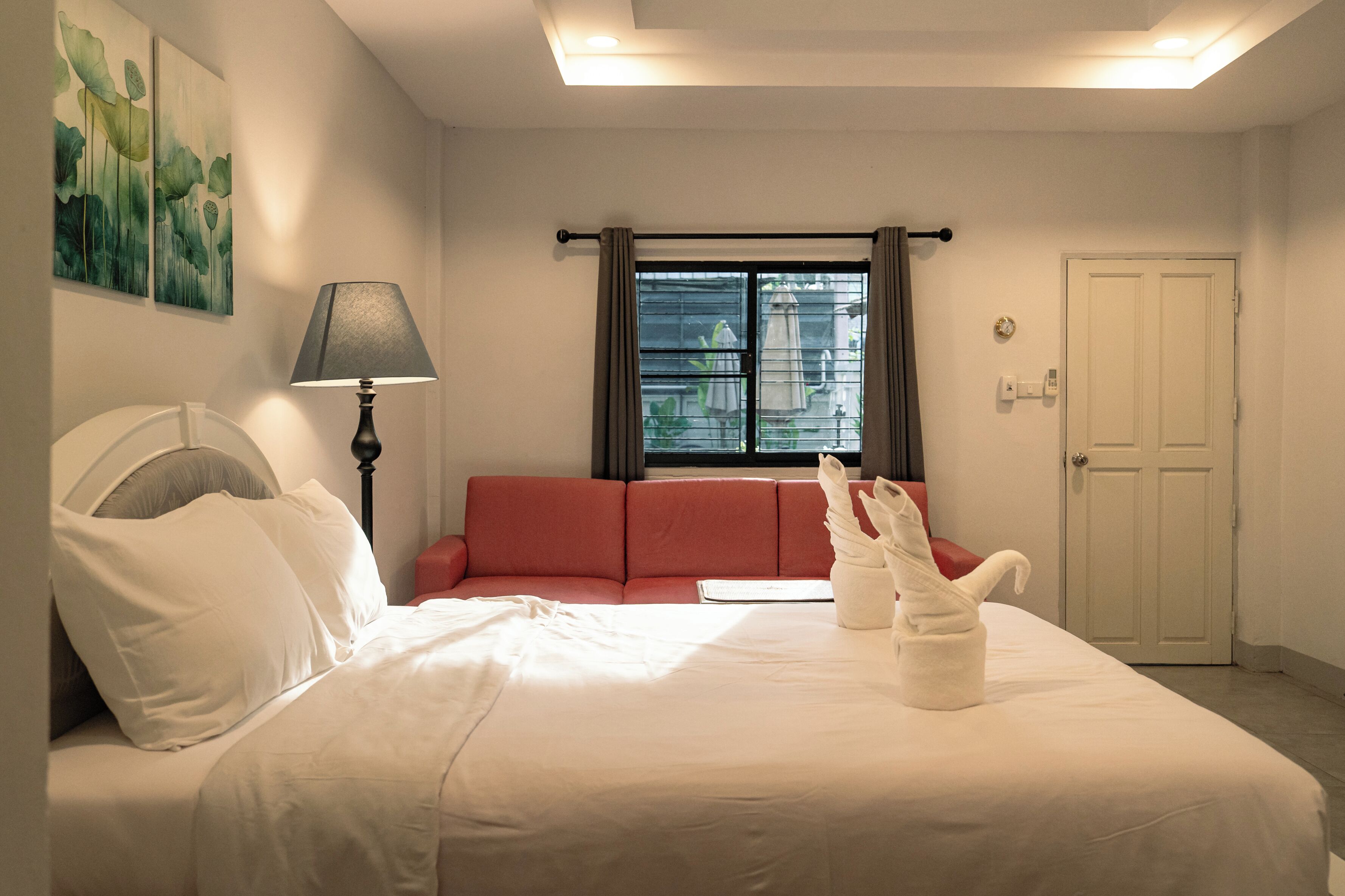 Ein Hotelzimmer mit einem Bett, einem roten Sofa, einer Lampe, einem Fenster mit Vorhängen und einer Tür.