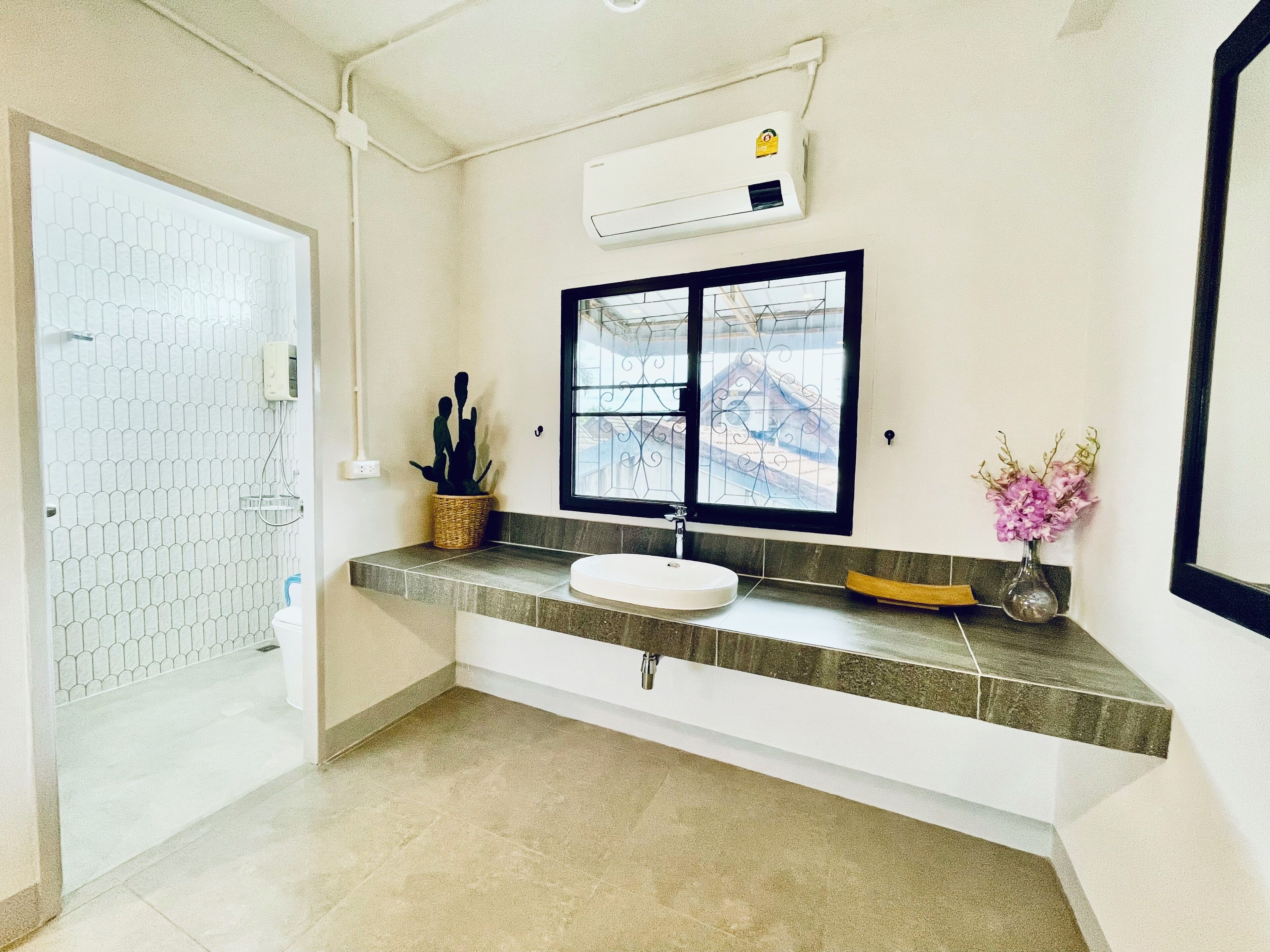 A bathroom with a white sink, a window with decorative iron bars, a potted plant, and a vase with flowers.