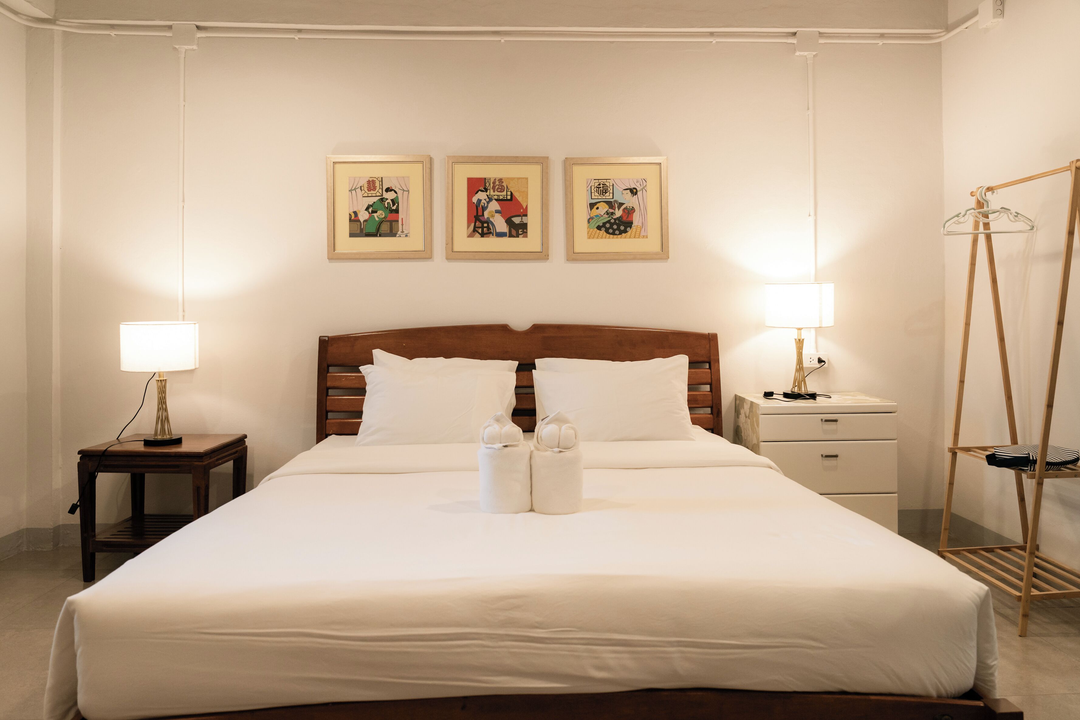 A neatly made bed with white linens, two bedside lamps, a wooden headboard, and three framed artworks on the wall.