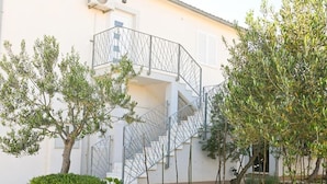 A building with a white exterior, a metal staircase with a railing, and surrounding greenery including trees and shrubs. - Apartment Zara (Marina)