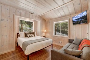 A bedroom with a bed, a nightstand, a lamp, a window, and a television.