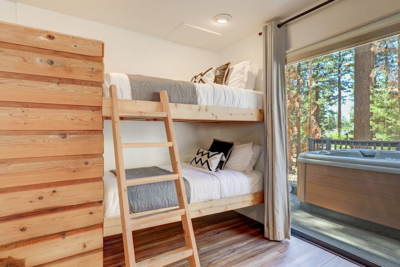 Un lit superposé avec une échelle, une fenêtre donnant sur les arbres et un jacuzzi.