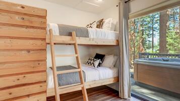 A bunk bed with a ladder, a window with a view of trees, and a hot tub.