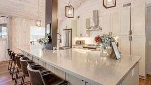 A modern kitchen with a large island, bar stools, stainless steel appliances, and pendant lighting. - Family Retreat | Master Suites-Hot Tub | Sleeps10 (Stateline)