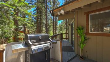 An outdoor grill area with a wooden deck, surrounded by tall trees.