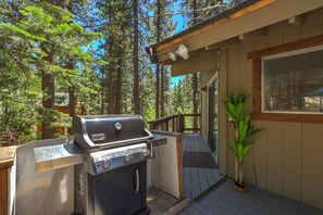An outdoor grill area with a wooden deck, surrounded by tall trees.