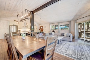 A spacious living area with a wooden dining table, sofas, and a large window offering a view of the outdoors. - Family Retreat | Master Suites-Hot Tub | Sleeps10 (Stateline)