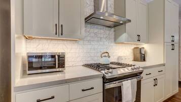 A modern kitchen with white cabinetry, a built-in microwave, a gas stove, and a stainless steel range hood.