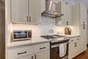 Une cuisine moderne avec des meubles blancs, un four à micro-ondes encastré, une cuisinière à gaz et une hotte en acier inoxydable.