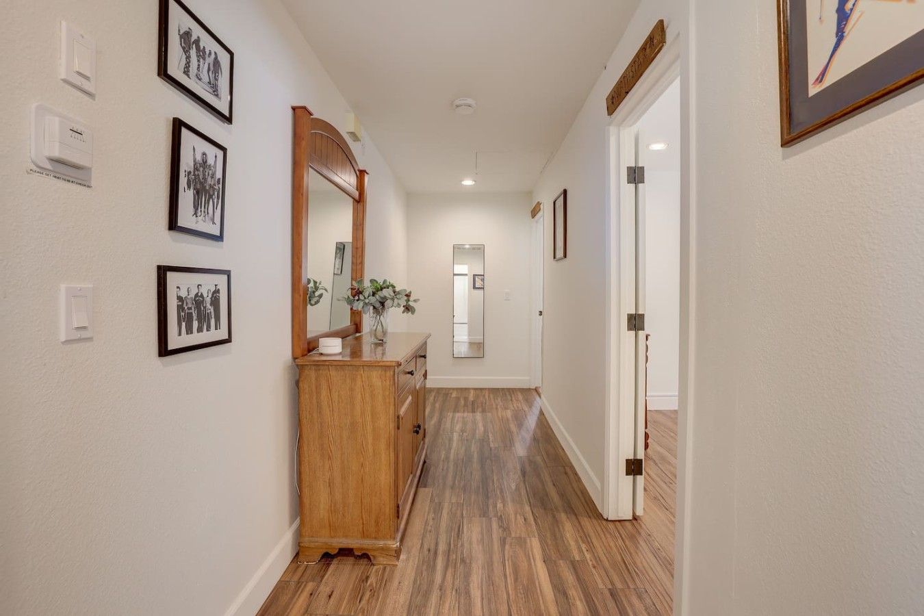 Un couloir doté d’un plancher en bois, d’une commode en bois et de tableaux encadrés accrochés aux murs.