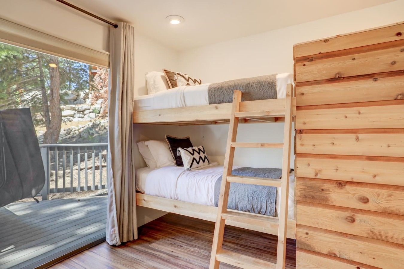 Un lit superposé avec une échelle, des murs en bois et une fenêtre avec des rideaux.