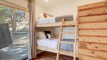A bunk bed with a ladder, wooden walls, and a window with curtains.