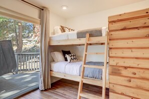 A bunk bed with a ladder, wooden walls, and a window with curtains.