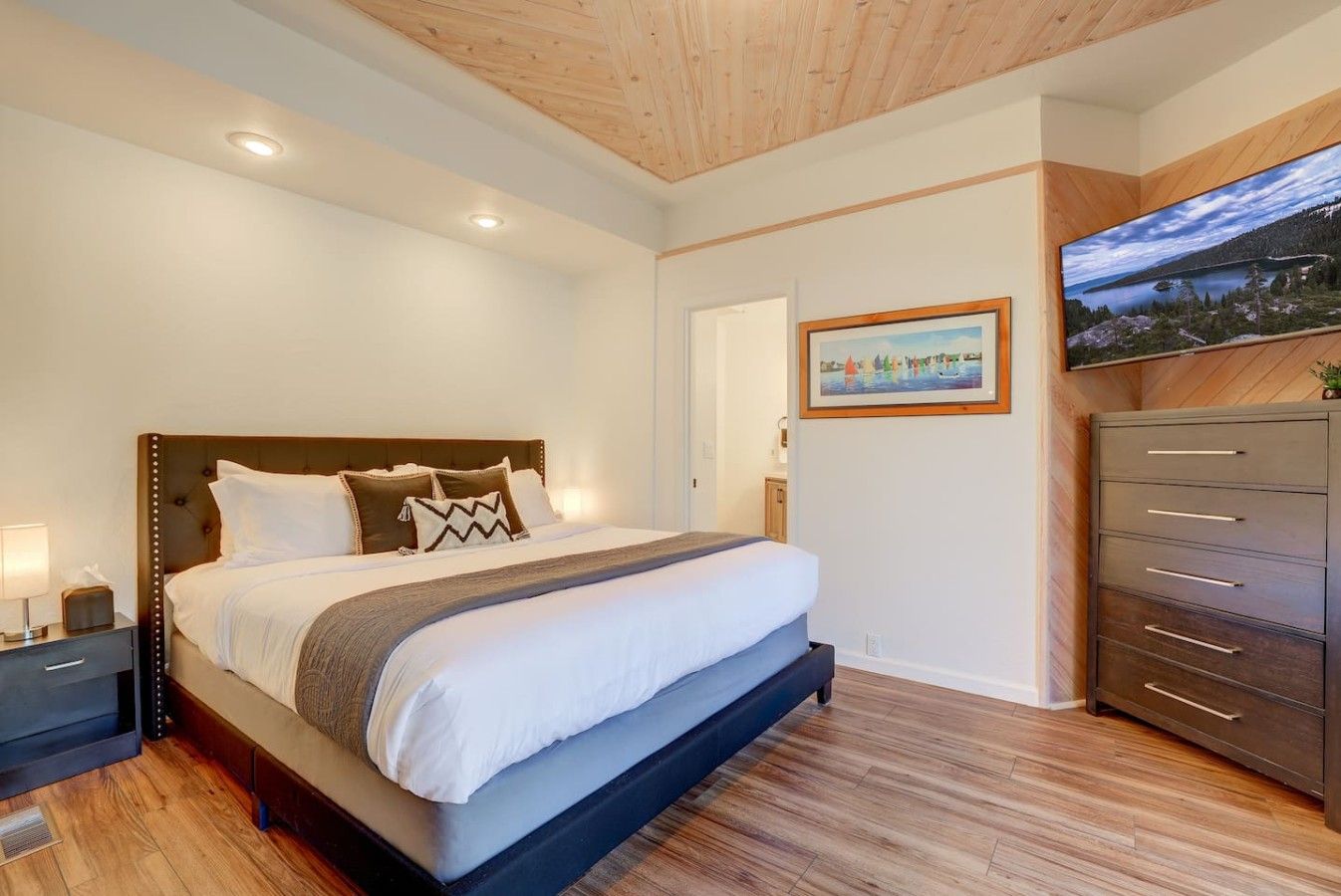 Quarto de hotel moderno com uma cama grande, piso de madeira, roupeiro embutido e uma pintura na parede.