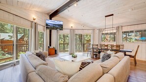 A spacious living room with a large sofa, a dining table, and a TV mounted on the wall. - Family Retreat | Master Suites-Hot Tub | Sleeps10 (Stateline)