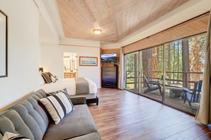 A modern interior with a wooden ceiling, a sofa, a bed, a TV, and a large sliding glass door leading to an outdoor deck.