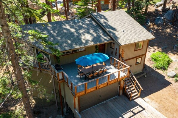 A two-story wooden cabin with a deck, a covered outdoor seating area, and a staircase leading to the upper level.