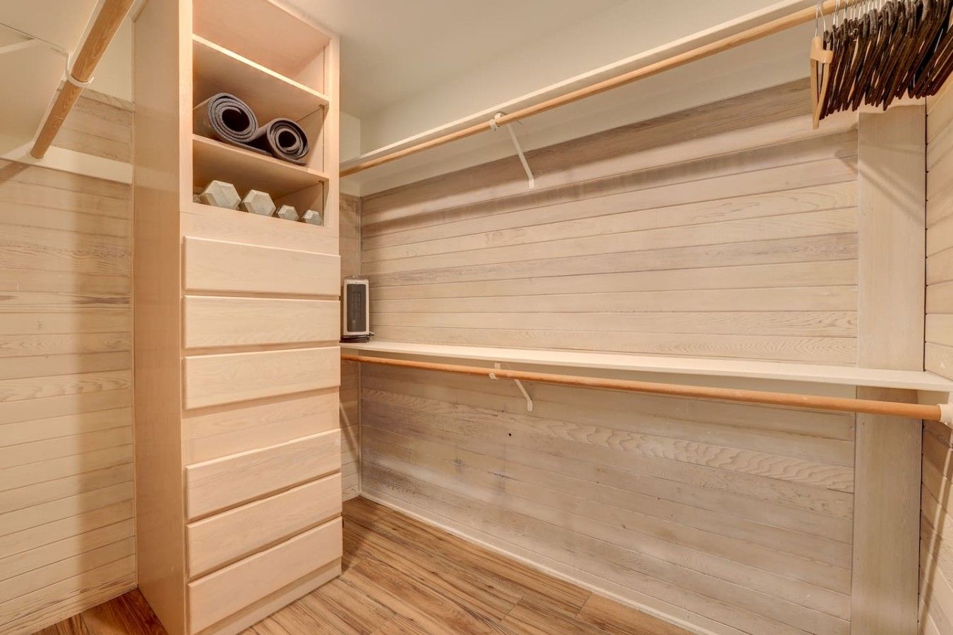 A walk-in closet with wooden flooring, a built-in shelving unit, and a hanging rod.