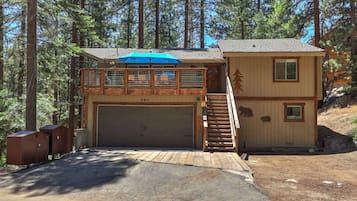 A two-story cabin with a garage, a covered outdoor seating area, and a staircase leading to the upper level.