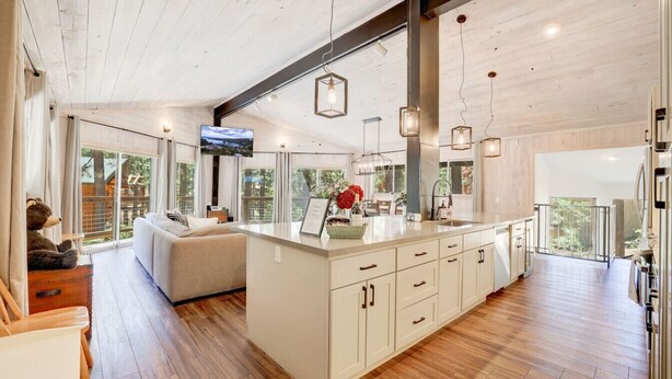 A spacious living area with a large island, wooden flooring, and a view of the outdoors. - Family Retreat | Master Suites-Hot Tub | Sleeps10 (Stateline)