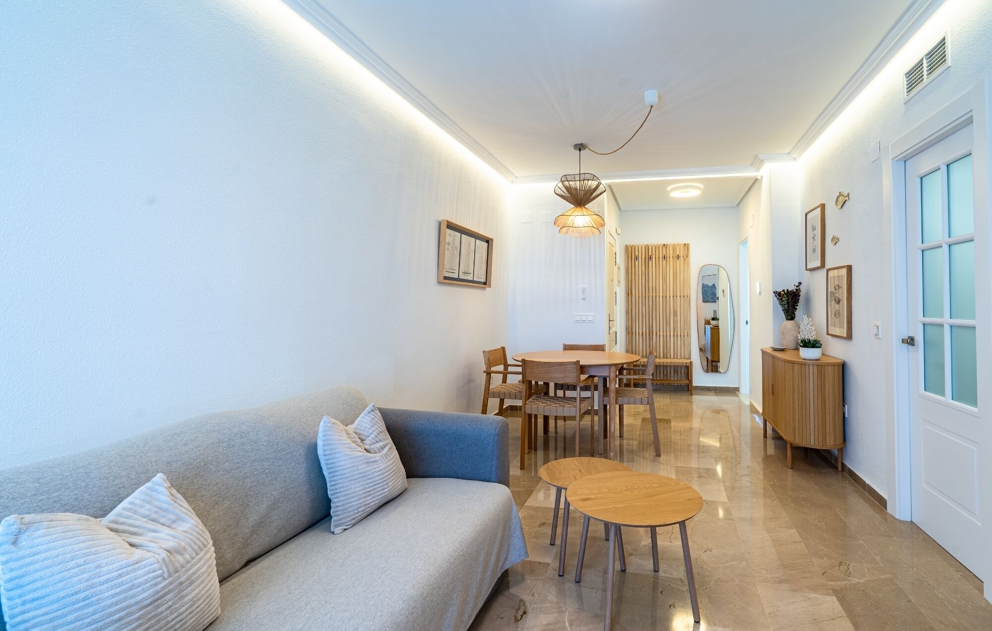A modern living room with a sofa, a coffee table, and a dining area with chairs and a table.