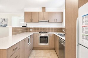 A compact kitchen with wooden cabinets, a built-in oven, a gas stove, and a refrigerator.