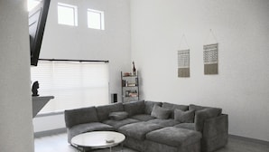 A modern living room with a grey sectional sofa, a round coffee table, and a bookshelf. - Luxury Home - near NRG, Medical Center, Downtown & Galleria (5 - 15 minutes) (Houston)