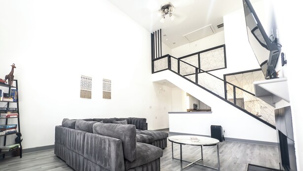 A modern living room with a grey sectional sofa, a round coffee table, and a staircase leading to an upper level. - Luxury Home - near NRG, Medical Center, Downtown & Galleria (5 - 15 minutes) (Houston)