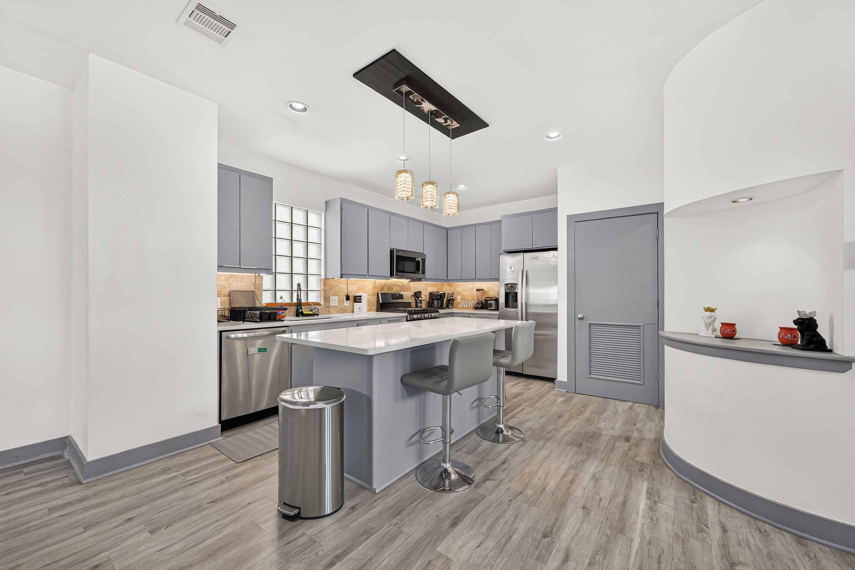 A modern kitchen with grey cabinets, stainless steel appliances, and a central island with bar stools.