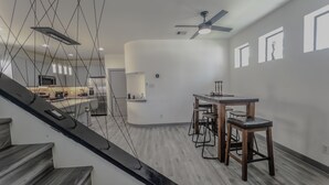 A modern kitchen with a central island, a dining area with wooden chairs, and a staircase with a black handrail. - Luxury Home - near NRG, Medical Center, Downtown & Galleria (5 - 15 minutes) (Houston)