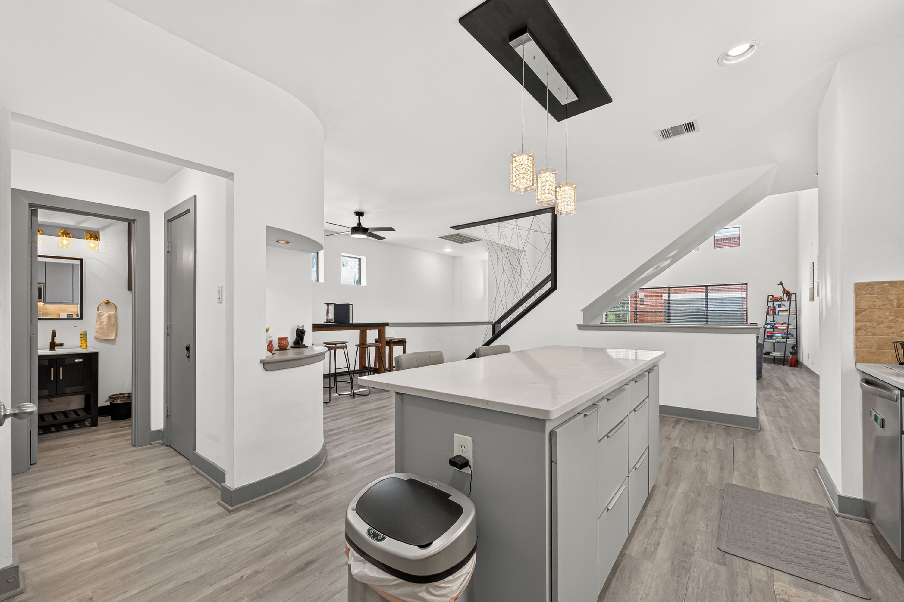 A modern kitchen with a central island, a dining area with bar stools, and a staircase leading to an upper level.