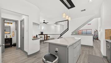 A modern kitchen with a central island, a dining area with bar stools, and a staircase leading to an upper level.