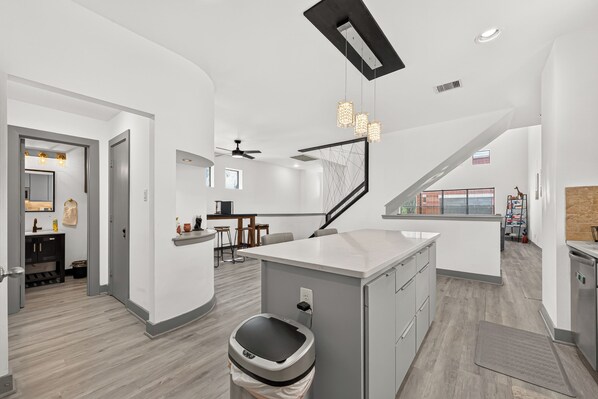 A modern kitchen with a central island, a dining area with bar stools, and a staircase leading to an upper level.
