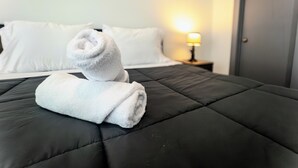 A neatly made bed with a black quilt, white pillows, and a rolled white towel on top. - Luxury Home - near NRG, Medical Center, Downtown & Galleria (5 - 15 minutes) (Houston)
