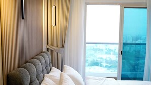 Ein modernes Schlafzimmer mit einem großen Bett, einem Kopfende mit besonderem Design und Blick auf eine Stadtlandschaft durch ein großes Fenster.