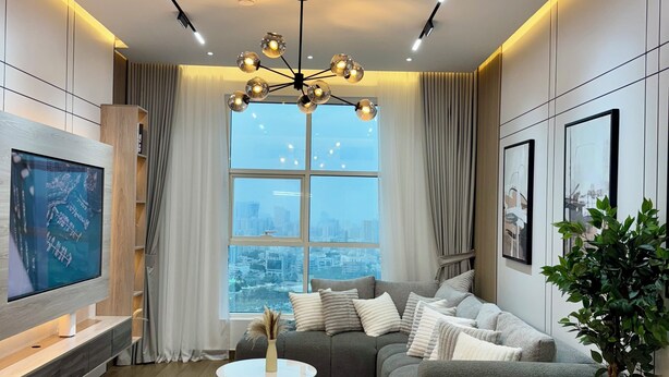 Ein modernes Wohnzimmer mit einem Ecksofa, einem Flachbildfernseher, einem runden Couchtisch und einem großen Fenster mit Blick auf die Stadt.