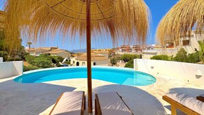 Un área de piscina con sillones de descanso y una sombrilla de paja.