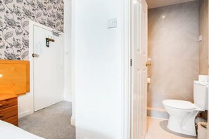 A bathroom with a toilet, a shower, and a door leading to a bedroom.