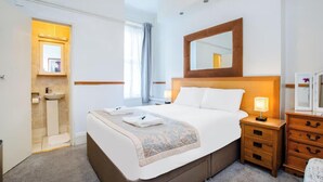 A hotel room with a large bed, bedside tables, a mirror, a dresser, and a bathroom with a sink and window.