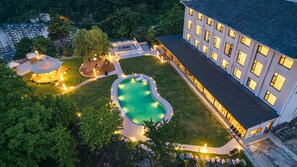 Vista aerea di un hotel con piscina, aree salotto all'aperto e un edificio grande con numerose finestre.