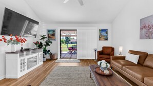 Ein modernes Wohnzimmer mit Fernseher, einem braunen Ledersofa, einer weißen Kommode und einem großen Fenster.