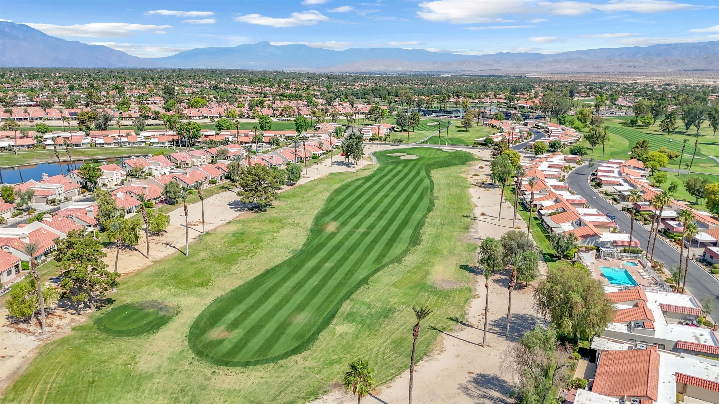A golf course with a well-maintained fairway, surrounded by residential areas with houses and a swimming pool.