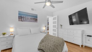 Ein Schlafzimmer mit Bett, Nachttischen, einem Schminktisch, einem Fernseher und einem Deckenventilator.