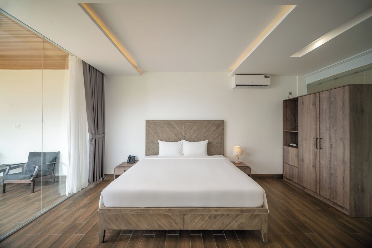 A modern hotel room with a large bed, wooden headboard, and a wardrobe.