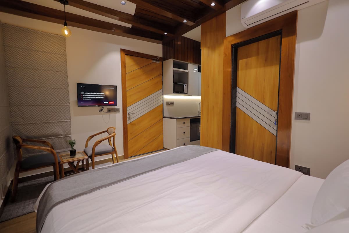 A hotel room with a bed, wooden wardrobe, a TV, and a small table with chairs.